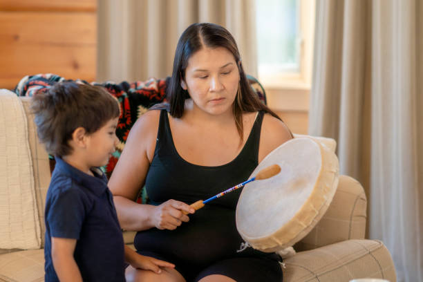 Expressive Arts - A young Indigenous mother is playing a traditional drum for her son at home. She is sharing her family's tradition and culture with her child.